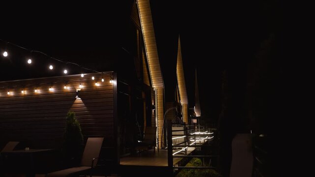 Row of modern wooden cottages with cozy illuminated terraces and string lights creating a warm and inviting atmosphere in a tranquil setting during a quiet evening, perfect for relaxation