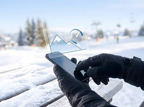 Person using tablet to analyze mountain ski slope data in snowy winter landscape.