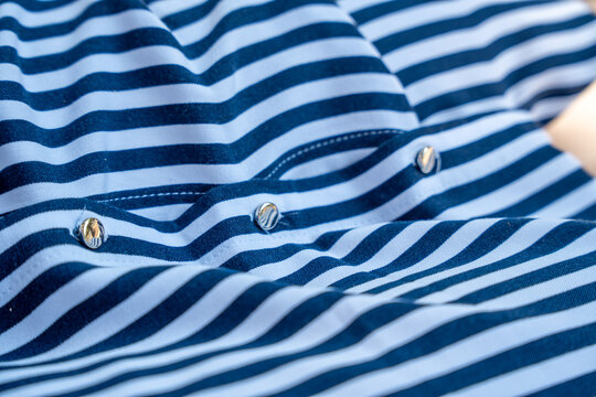 Close up of a navy and white striped shirt with metal snap buttons along the placket and soft folds, concept of nautical fashion, casual summer clothing and garment detail