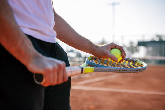 Tennis player holding racket and ball in mid section close up view