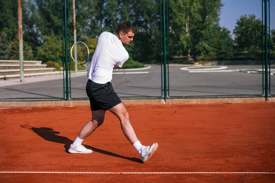Tennis player completing two handed backhand swing rotation on clay court