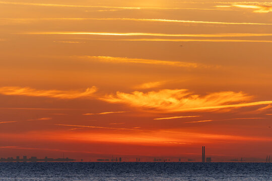 Luc-Sur-Mer, France - 08 08 2022:  Colorful sunrise over the sea and port of Le Havre far away