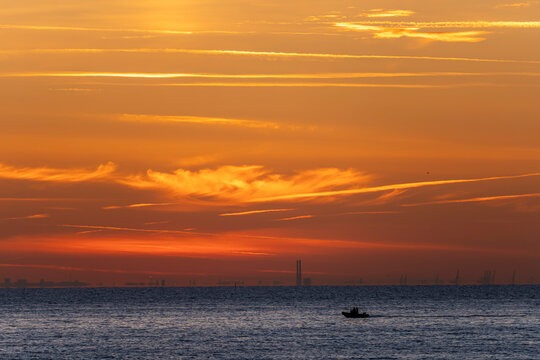 Luc-Sur-Mer, France - 08 08 2022:  Colorful sunrise over the sea, a fisherman's boat and port of Le Havre far away