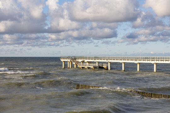 Pier extending over rough sea with waves under cloudy sky in daylight