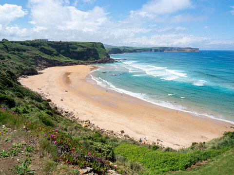 Scenic Los Locos Beach in Suances Spain - A breathtaking high-angle view of the golden sandy shore and turquoise waves at Los Locos Beach, surrounded by lush green cliffs in Suances.