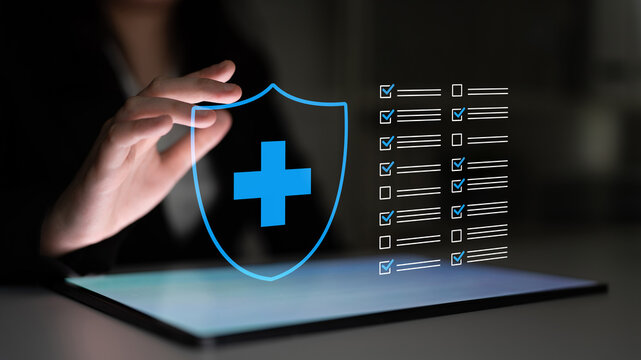 A person interacts with a digital health shield symbol on a tablet, symbolizing security and management in healthcare within a dark, modern environment. Cyphers