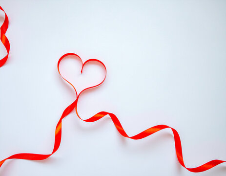 Red satin ribbon curved into a heart shape with flowing wavy ends on a clean white background, creating a romantic Valentine's Day concept with plenty of copy space for greetings.