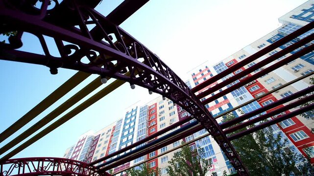 Low angle view of modern apartment house displays vibrant facades through decorative metal pergola. Architectural steel structure frames urban residential quarter on clear sunny afternoon.