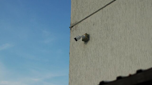 Modern cctv unit mounted on exterior concrete wall watches surrounding territory during sunny day. Reliable security device stands fixed providing protection against unexpected intrusions.