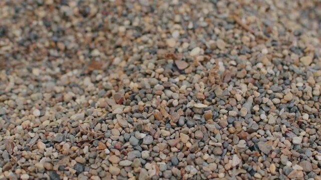 Coarse gravel dropping down onto stone pile creates subtle movement across frame. Natural mineral grains accumulate gently while sharp detailed texture covers entire visual space as loose stones