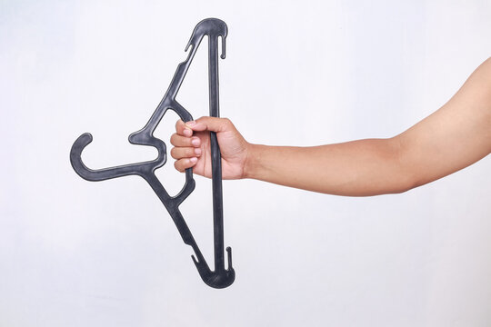 Person holding black plastic clothes hanger against white background