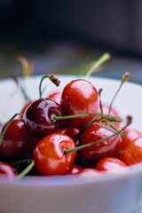 Fresh juicy ripe red cherries with glistening water drops sitting inside a white ceramic bowl during daytime lighting © Ghayas
