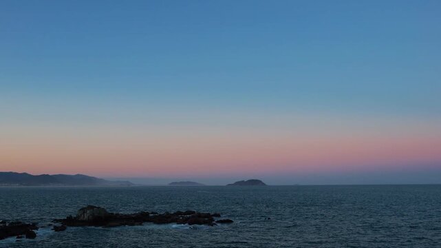 Scenic seascape of a rocky coastline under a pastel pink and orange sunset sky
Distant island on the horizon with a colorful late afternoon gradient sky
Tranquil ocean view with dramatic coastal rocks