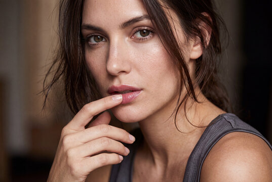 Seductive close-up portrait of a beautiful young woman touching her lips with intense gaze.