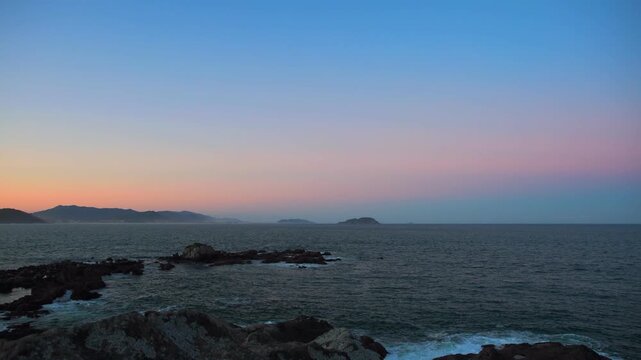 Scenic seascape of a rocky coastline under a pastel pink and orange sunset sky
Distant island on the horizon with a colorful late afternoon gradient sky
Tranquil ocean view with dramatic coastal rocks
