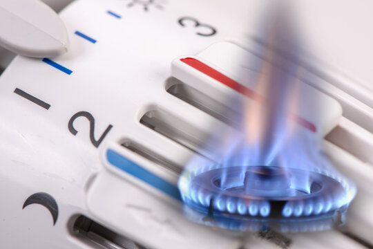 Eine Gasflamme brennt vor dem Thermostat einer Heizung - FOTOMONTAGE