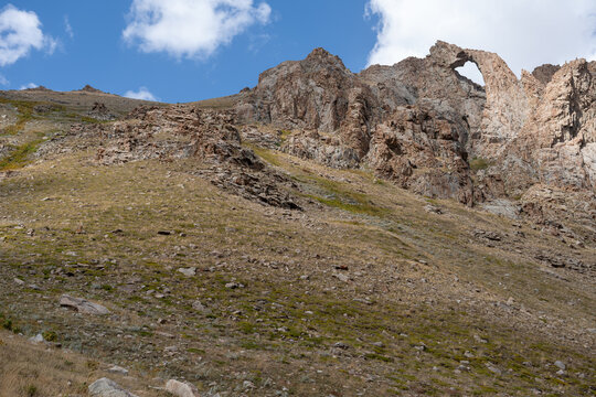 Dramatic Rocky Mountain Landscape with a Natural Rock Arch Under a Blue Cloudy Sky.