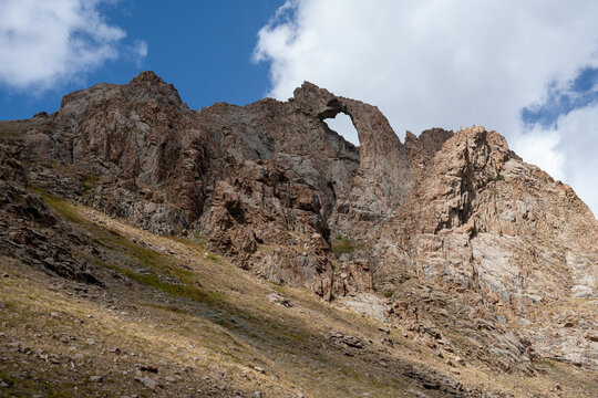 Dramatic Rocky Mountain Landscape with a Natural Rock Arch Under a Blue Cloudy Sky.