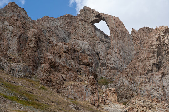Dramatic Rocky Mountain Landscape with a Natural Rock Arch Under a Blue Cloudy Sky.