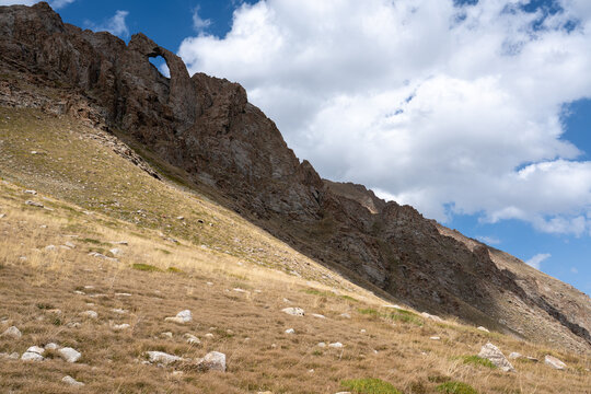Dramatic Rocky Mountain Landscape with a Natural Rock Arch Under a Blue Cloudy Sky.