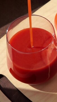 Thick fresh tomato juice being poured into a clear glass in a bright home kitchen setting, highlighting plant-based food consumption