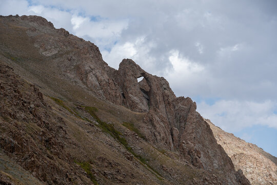 Dramatic Rocky Mountain Landscape with a Natural Rock Arch Under a Blue Cloudy Sky.
