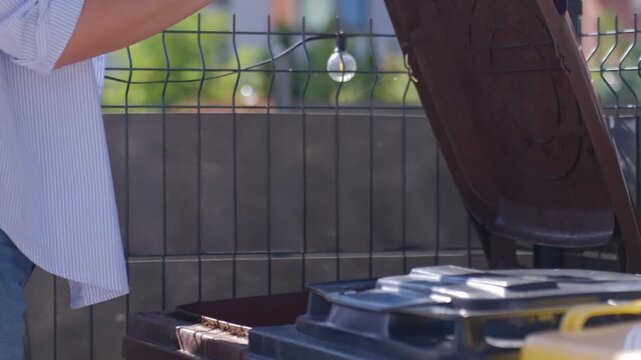 Woman opens brown waste bin, throws banana peel inside and closes lid. Concept of organic waste sorting and compostable food disposal