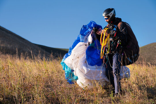 Paraglider holding equipment in grassy field under blue sky