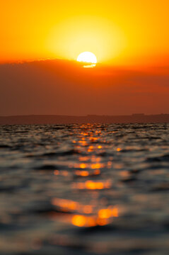 Sunset over ocean with sun setting behind clouds
