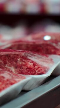 Fresh raw beef cuts rest neatly inside plastic packaging within supermarket butcher case, displaying red marbling while cold refrigerated retail shelf keeps raw meat items organized.