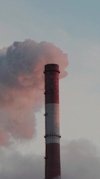 Factory smokestack discharges thick exhaust into open air as twilight glow highlights rising plume, demonstrating industrial air pollution and atmospheric carbon footprint effectively.