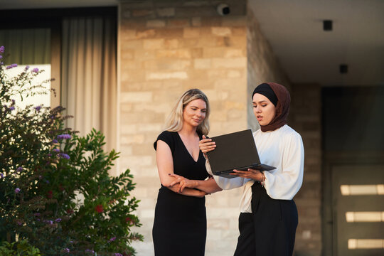 Multicultural Female Colleagues Reviewing Laptop Presentation Outside Modern Office Building