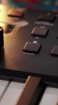 Finger pushes panic switch on black synthesizer interface under warm overhead spotlight. Creative sound artist manages audio gear controls during studio recording and composing session.