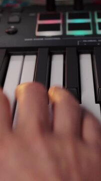 Musician fingers press black and white keys on digital midi keyboard synthesizer controller. Electronic audio creator plays melodic chords and adjusts sound controls during recording session.