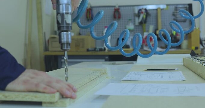 A furniture maker or furniture designer in blue workwear marking and preparing particle board parts on a workbench in a furniture factory workshop. Wooden furniture assembly.