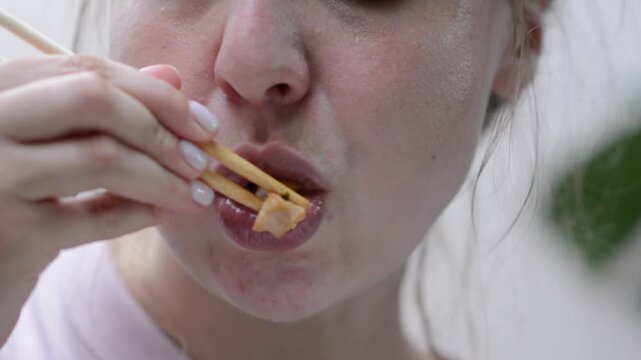 Close-up footage focusing only on a woman&rsquo;s face as she eats udon noodles with chicken. 