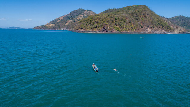 Aerial view of the Gulf of Fonseca near Meanguera Island, showing calm blue waters, a small boat, a swimmer, and rugged tropical hills along the coastline. 