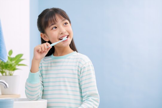 Young Asian girl brushing teeth with toothbrush in bright bathroom. Child practicing daily oral hygiene routine with copy space