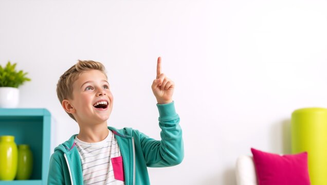 Excited boy pointing finger up at copy space. Happy young child having a creative idea in bright room