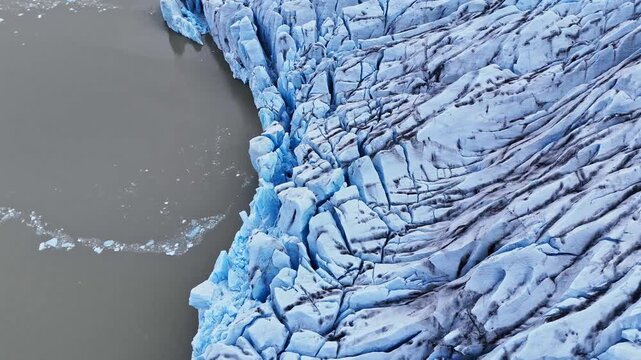 Aerial view of Svinafellsjokull glacier with deep blue crevasses and ice formations meeting the dark glacial lagoon Svinafellsjokull Glacier, Sveitarfelagid Hornafjordur, Iceland.