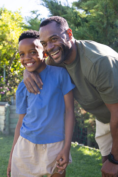 African American father and youth son leaning, smiling in sunlit garden, son holding folded paper