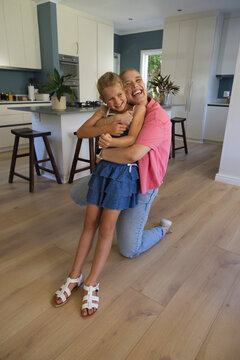 Female adolescent and child kneeling on light wood floor hugging, laughing by island plants