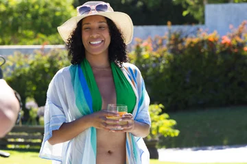 African American woman standing poolside in green swimwear straw hat holding orange cocktail glass © WavebreakMediaMicro