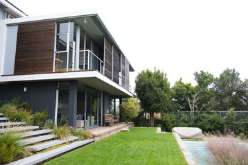 Obraz premium Modern two-story house is showing wood cladding and balcony over timber deck in suburban backyard