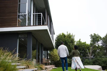 African American couple walking on lawn toward modern glass home, passing stone steps, copy space © WavebreakMediaMicro