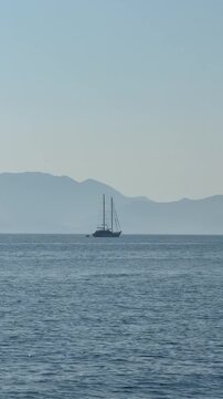 Two-masted sailing ship silhouette on calm blue sea against misty mountains, Ionian Sea, Greece