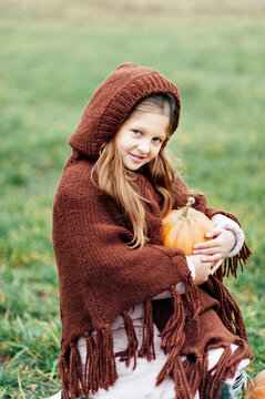 Happy little girl on pumpkin patch on cold autumn day, with a lot of pumpkins for Halloween or thanksgiving.