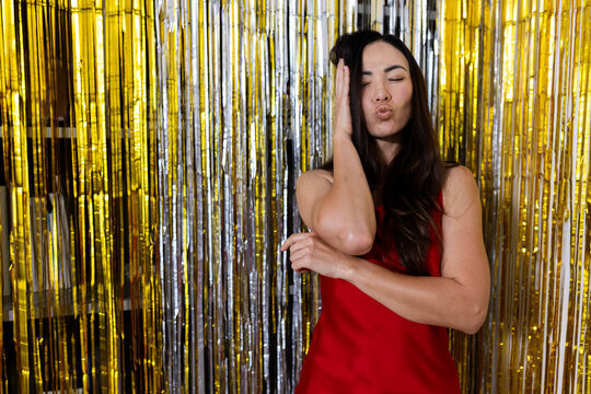 Woman posing and blowing kiss in sleeveless red dress at party booth with metallic foil curtain
