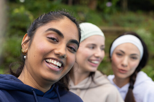 Diverse female friends smiling and leaning together in park with navy hoodie and headbands