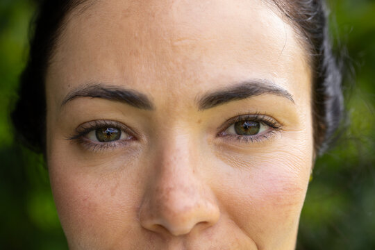 Female face filling frame, showing textured skin, pores and freckles, eyes gazing at camera in park